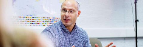 Male lecturer with glasses explaining something with a world map in the background