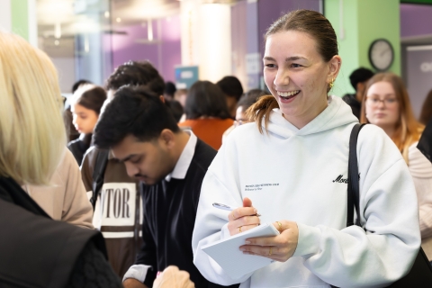 A female student is speaking to a member of staff in the Careers and Employability Centre while writing notes.